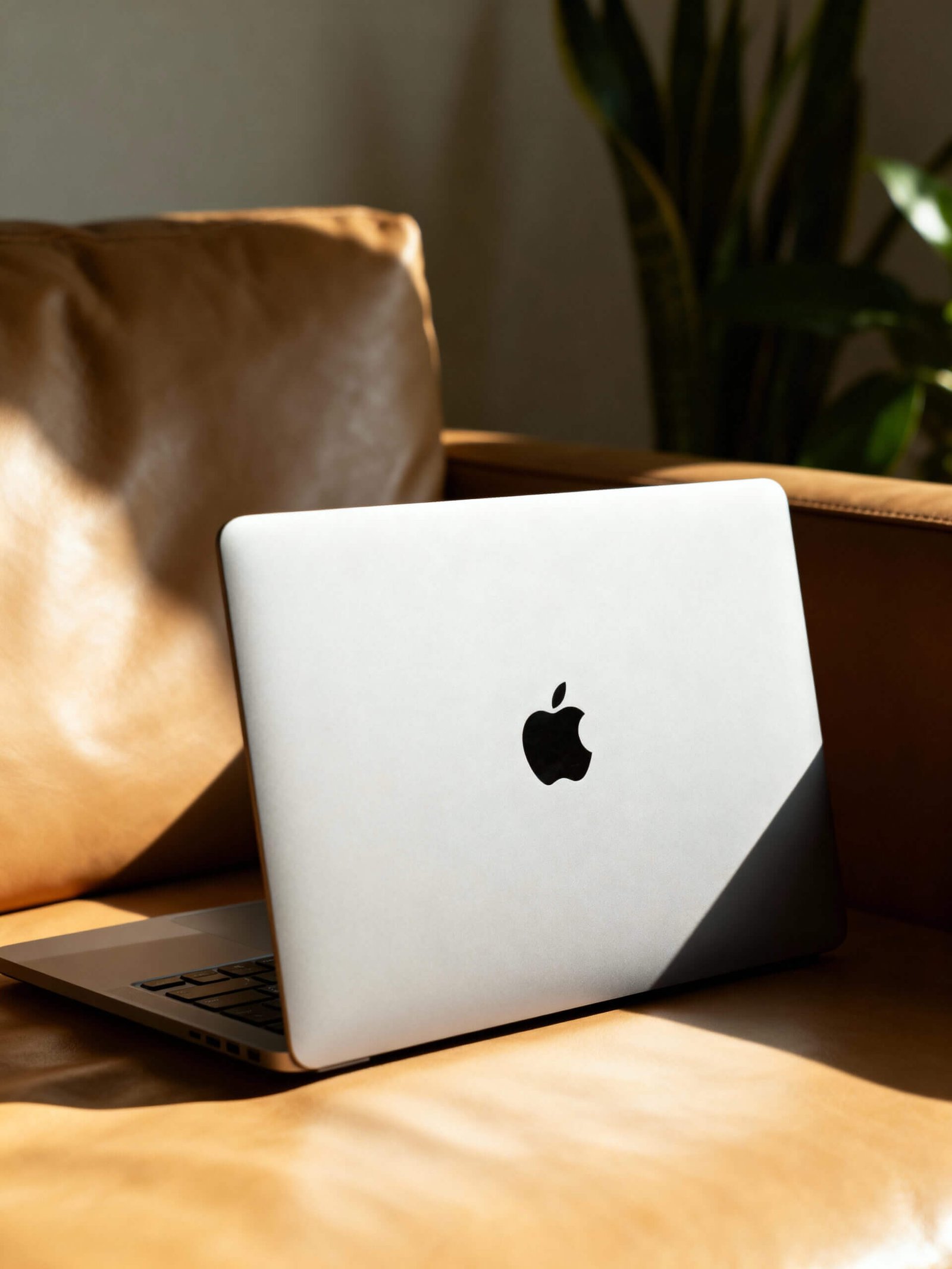 http://Laptop%20auf%20einer%20Ledercouch,%20mit%20sichtbarem%20Apple-Logo,%20umgeben%20von%20natürlichem%20Licht%20und%20Pflanzen%20im%20Hintergrund.
